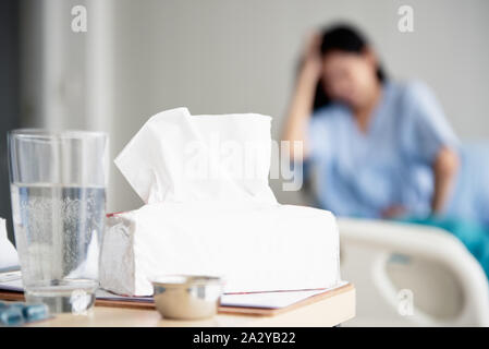 Das Mädchen im Bett des Krankenhaus sitzen. Sie hatte Kopfschmerzen, Bauchschmerzen und hatte eine Krankheit. haben die Medizin, die ein Glas Wasser und Gewebe am Tisch. Stockfoto