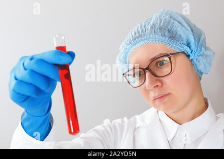 Eine Wissenschaftlerin mit Brille ist Experimentieren im Labor und hält ein Reagenzglas mit roter Flüssigkeit in den Händen. Stockfoto