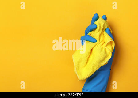 Eine Hand in einem schützenden blau Handschuh hält einen gelben Lappen auf einem gelben Hintergrund. Stockfoto