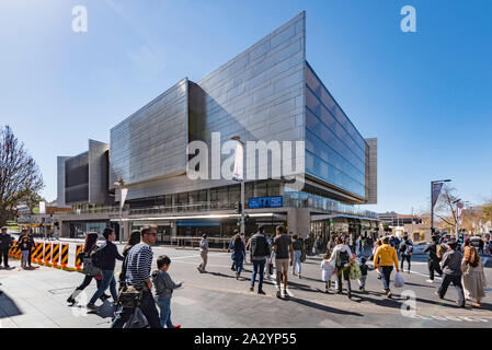 Eine große Gruppe von Menschen Überqueren einer Straße in Richtung Bahnhofshalle (Kulturzentrum) Gebäude in der Sydney Vorort von Chatswood in Australien Stockfoto