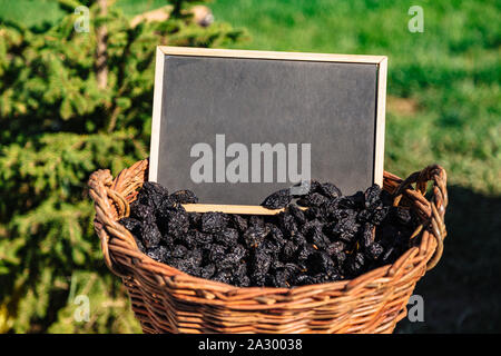 Korb voller ovaler schwarzer Pflaumen auf dem Feld Stockfoto