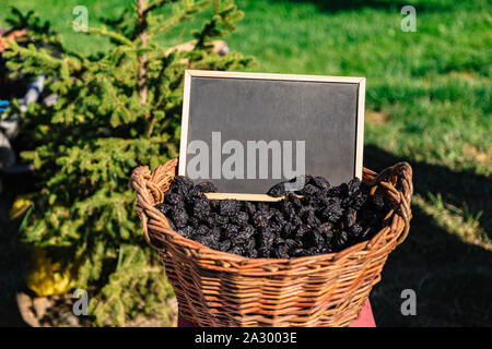 Korb voller ovaler schwarzer Pflaumen auf dem Feld Stockfoto