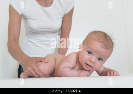 Portrait of smiling baby mit großen Augen liegen auf Wickeltisch und Frau ihn von hinten Stockfoto