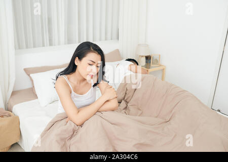 Wir haben ein Problem. Junge umgekippt Mädchen sitzt auf der Kante des Bettes, gegen ihren Freund, im Bett zu liegen. Stockfoto