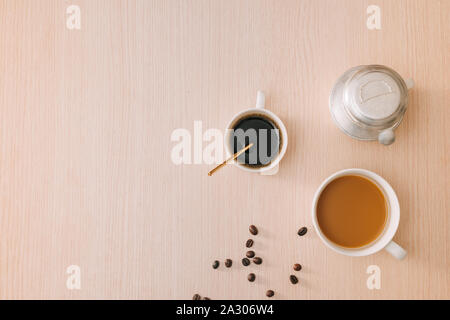 Tassen Kaffee mit Kaffeebohnen und vietnamesische Phin Filter auf Holz- Hintergrund Stockfoto