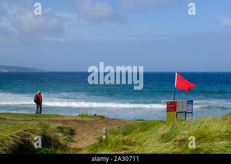 Eine rote RNLI Lifeguards Warnung Fahne über den Strand fliegen an Godrevy in Cornwall. Stockfoto