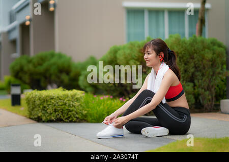 Asiatische schöne Frau sitzend für Entspannen und versuchen, Schnürsenkel in Font ihres Hauses im Dorf, glücklich und Lächeln am Morgen bei Tageslicht. Sport Fitnes Stockfoto