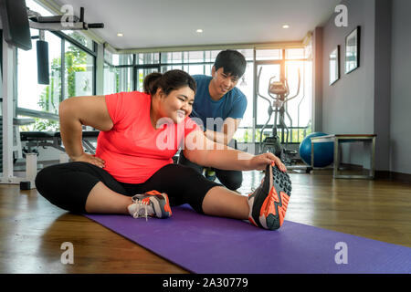 Zwei asiatische Trainer Mann und übergewichtige Frau zusammen Training zu dehnen im modernen Fitnessraum, glücklich und Lächeln während des Trainings. Dicke Frauen kümmern sich um Gesundheit. Stockfoto