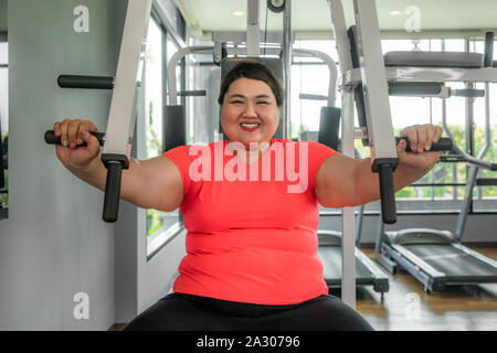 Asiatische übergewichtige Frau spielen Fitnessgeräte zur Ausübung ihrer boday allein in der Turnhalle bauen, glücklich und Lächeln während des Trainings. Dicke Frauen kümmern sich um die Gesundheit Stockfoto