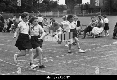 1950, historische, Grundschule, Sport, Schülerinnen, die sich an einem Dreibeinigen laufende Rennen außerhalb in einer Rasenfläche, England, UK. Ein 3-legged Race ist ein Spaß, die Veranstaltung mit Paaren der Kinder laufen mit dem linken Bein auf das rechte Bein eines anderen Runner festgeschnallt. Stockfoto