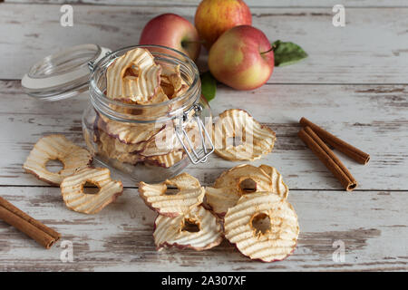 Getrocknete äpfel Chips in Schale mit frischen roten Äpfel und Zimtstangen auf Tisch. Stockfoto