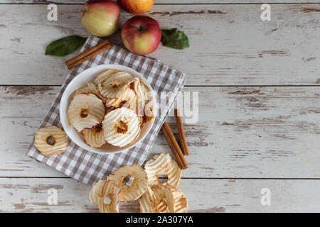 Getrocknete äpfel Chips in Schale mit frischen roten Äpfel und Zimtstangen auf Tisch. Stockfoto