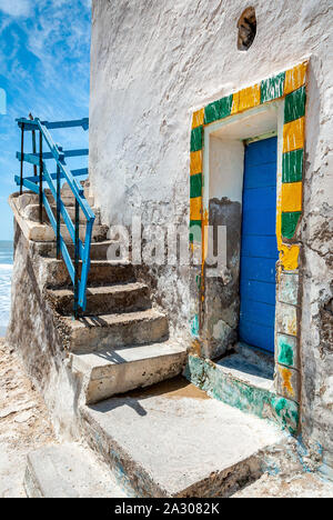 Gelbe und grüne Rahmen einer blauen Tür am Fuße einer Außentreppe auf ein altersschwaches weißes Gebäude in Sidi Kaouki, Marokko Stockfoto