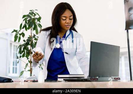 Schwarze weibliche Arzt bei der Arbeit im Büro, zu Laptop suchen. Schöne afrikanische amerikanische Frau Arzt oder Krankenschwester, die auf einem Laptop Computer in der modernen Stockfoto