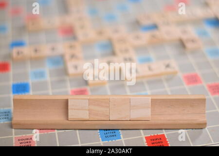 4 leere Holz- scrabble Tiles auf eine Kachel-Rack, für die Sie in Ihrem eigenen Wort zu füllen. Im Hintergrund ein Vintage board, unscharf, mit Kopie Raum Stockfoto