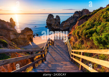 Sonnenaufgang am Camilo Strand in Lagos, Algarve, Portugal. Holzsteg zum Strand Praia do Camilo, Portugal. Malerischen Blick auf Praia do Camilo bea Stockfoto