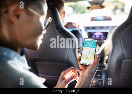 Afrikanische Frau mit Car Sharing App beim Sitzen im Auto. Stockfoto