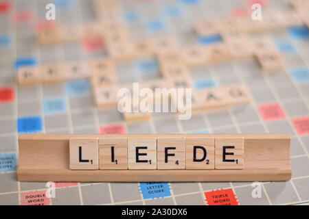 Das niederländische Wort "LIEFDE" (auf Deutsch: "Liebe") in Holz- Scrabble Fliesen auf einem Baugruppenträger. Der Hintergrund ein Vintage board, unscharf, mit Kopie Raum Stockfoto