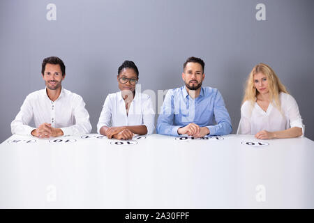 Multirassischen zuversichtlich Richter sitzen auf Stuhl mit Punkten auf dem Tisch gegen die Wand Stockfoto