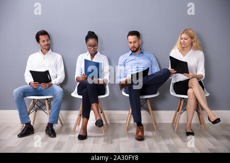 Multiethnischen Geschäftsleute sitzen auf Stühlen in der Reihe warten auf Job Interview gegen graue Wand Stockfoto