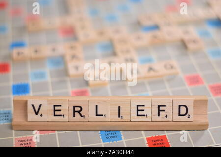 Das niederländische Wort "rliefd" (auf Deutsch: "in der Liebe") in Holz- Scrabble Fliesen auf einem Baugruppenträger. Der Hintergrund ein Vintage board, unscharf, mit Kopie Raum Stockfoto