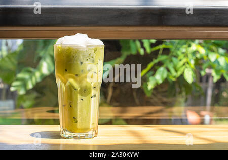 Eistee grüner Tee im Glas auf dem hölzernen Tisch Hintergrund Glasfenster und Baum. Stockfoto