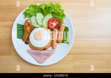 Amerikanische gebratener Reis mit Wurst, Schinken, Eier, Huhn, Tomaten, Gurken, auf Bananenblättern in einem weißen Teller. Stockfoto
