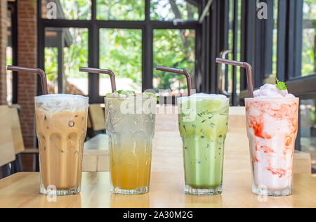 Eiskaffee, Honig Lemon Soda, Eistee grüner Tee und Erdbeere Smoothie in Glas auf dem hölzernen Tisch Hintergrund Glasfenster und Baum. Stockfoto