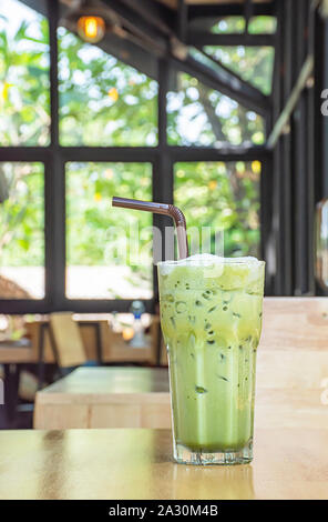 Eistee grüner Tee im Glas auf dem hölzernen Tisch Hintergrund Glasfenster und Baum. Stockfoto