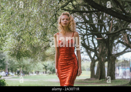 Porträt der schönen blonden Mädchen im roten Kleid mit Pailletten in Park Stockfoto