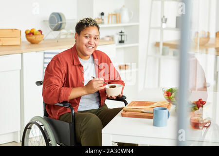 Portrait von jungen behinderten Frau sitzt im Rollstuhl und lächelnd an der Kamera beim Frühstück in der Küche Stockfoto