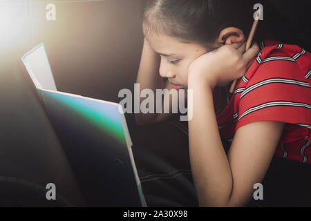 Kleines Mädchen mit Hausaufgaben auf dem Schlafsofa unter Licht zu Hause. Bildung Konzept. Stockfoto