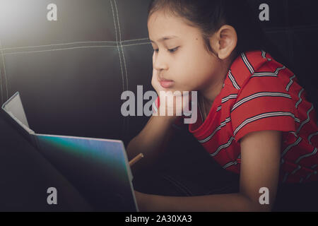 Kleines Mädchen mit Hausaufgaben auf dem Schlafsofa unter Licht zu Hause. Bildung Konzept. Stockfoto