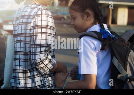 Mutter und Tochter gehen Hand in Hand unter Sonnenlicht in die Schule. Stockfoto