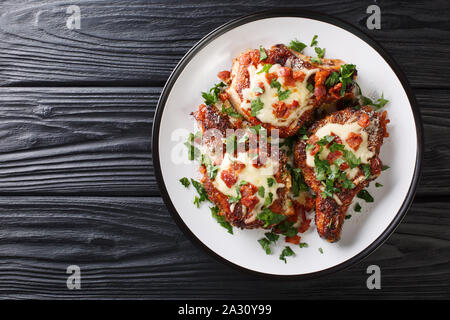 Würzig gebratene Schweinekoteletts mit geschmolzenem Käse und Speck closeup auf einem Teller auf den Tisch. Horizontal oben Ansicht von oben Stockfoto