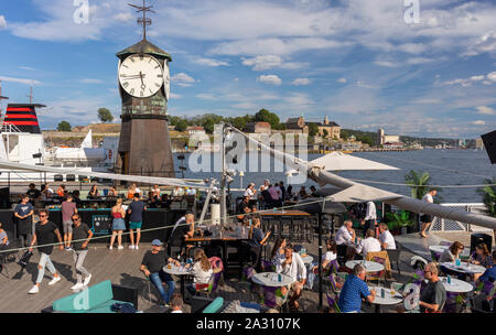 OSLO, Norwegen - Leute im Restaurant auf Oslo Waterfront, und Uhrturm bei Aker Brygge Dock. Stockfoto