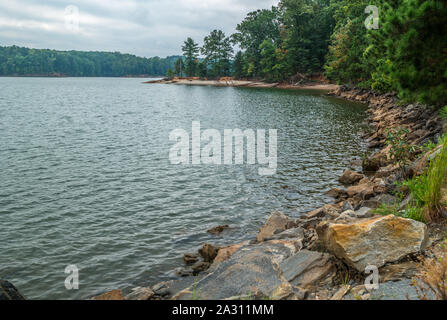 Eine trübe bedecktem Himmel auf dem See Küste mit Felsen und Geröll Futter der Wald, den See im Hintergrund umgibt im frühen Herbst Stockfoto