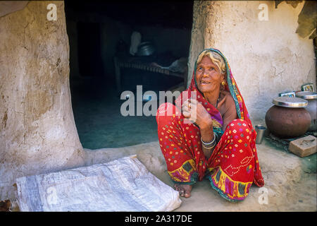 Eine alte indische Frau vor dem Eingang zu Ihrer Lehmhütte sitzen, Kleidung einen bunten Sari und einige Schmuckstücke. Stockfoto