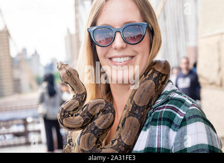 Junge, 20er Jahre weibliche Touristen mit eine große Schlange um den Hals auf der Brooklyn Bridge In New York City, USA. Stockfoto