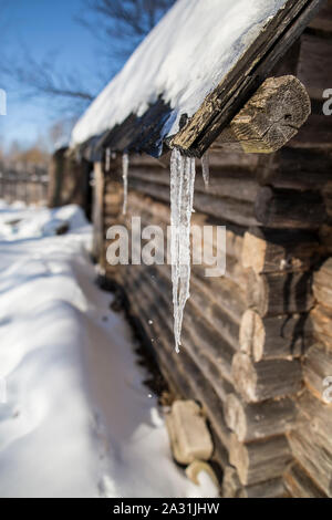 Eiszapfen hängen vom Dach der alten Blockhütte und tropfenden Frühling fällt, an einem sonnigen Tag im Dorf. Stockfoto