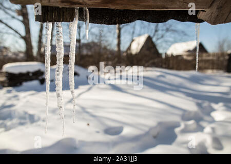 Eiszapfen hängen vom Dach der alten Hütte und tropfenden Frühling fällt, an einem sonnigen Tag im Dorf. Stockfoto