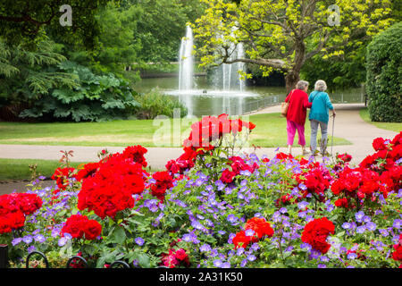 Zwei alte ältere Damen gehen Arm in Arm durch die jephson Gärten Gärten in Royal Leamington Spa Warwickshire, England Stockfoto