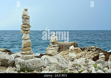 Cairns aus Steinen am felsigen Ufer der Adria in Kroatien. Vor dem Hintergrund der blaue Himmel, Meer und Segelboot, am Horizont. Stockfoto