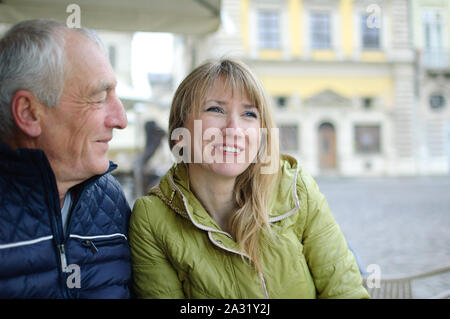 Gut aussehender älterer Mann begrüßt seine junge blonde Frau Ausgabe Zeit zusammen im Freien in der antiken Stadt im frühen Frühjahr oder Herbst. Stockfoto