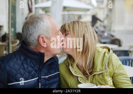 Gut aussehender älterer Mann begrüßt seine junge blonde Frau Ausgabe Zeit zusammen im Freien in der antiken Stadt im frühen Frühjahr oder Herbst. Stockfoto