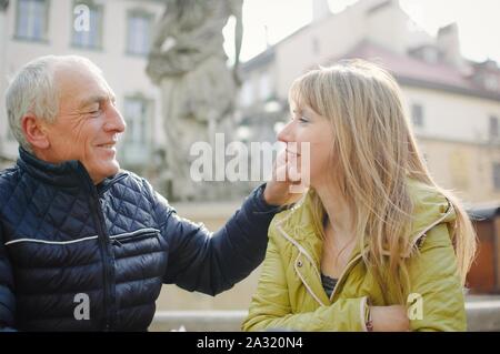 Gut aussehender älterer Mann begrüßt seine junge blonde Frau Ausgabe Zeit zusammen im Freien in der antiken Stadt im frühen Frühjahr oder Herbst. Stockfoto