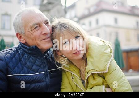 Gut aussehender älterer Mann begrüßt seine junge blonde Frau Ausgabe Zeit zusammen im Freien in der antiken Stadt im frühen Frühjahr oder Herbst. Stockfoto