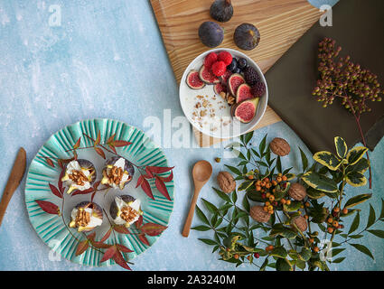 Ansicht von oben Grüne Platte mit frischen Feigen gefüllt mit Frischkäse und Muttern. Schüssel Naturjoghurt mit Feigen, Himbeeren und Brombeeren. Blätter... Stockfoto