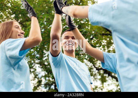 Freiwilligenarbeit. Die jugendlichen Freiwilligen im Freien gemeinsam mit hoher fünf Mission beenden Lachen heiter - Ansicht von unten Stockfoto