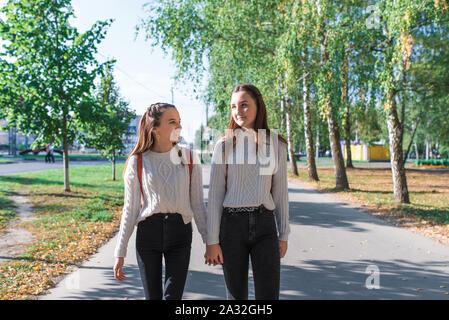 Jugend Mädchen Pullover mit Rucksäcken hinter im Sommer Herbst Frühling in der Stadt, am Wochenende nach der Schule. Hintergrund Bäume Gras, Park. Glücklich Stockfoto